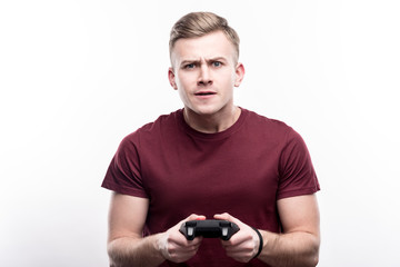 Focused on playing. Charming fair-haired young man holding a video game controller and playing a game, being focused