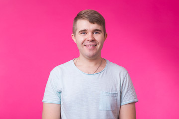 Funny young man looking at camera and smiling on pink background.