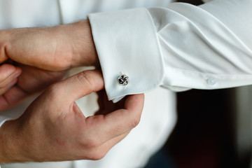 A man wears buttons of cufflinks on the sleeves of the white shirt. Businessman getting dressed by...