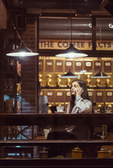 Young pretty brunette girl wears grey sweater have pleasant conversation by smartphone sitting near cafe window