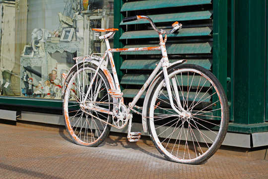 Shabby white bicycle standing near the shop outdoors