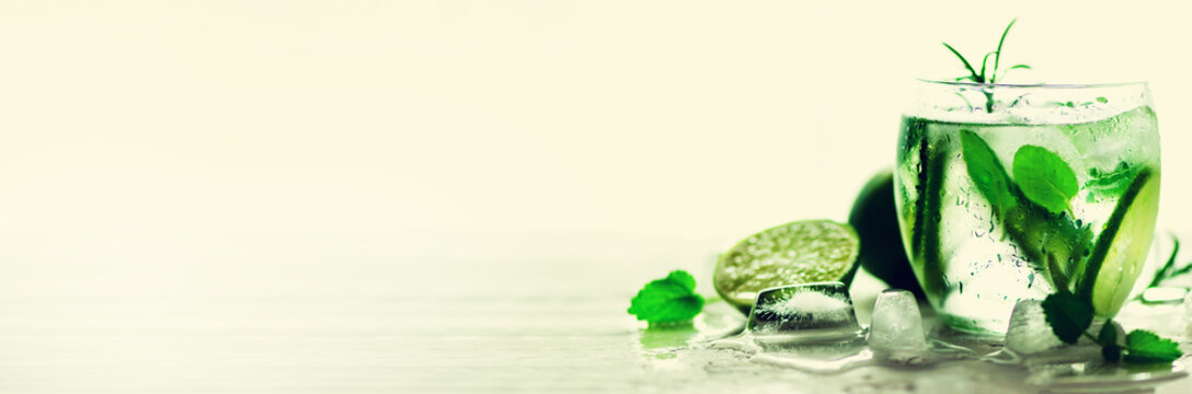 Homemade lime lemonade with cucumber, rosemary and ice, white background. Cold beverage, detox water. Copyspace. Banner