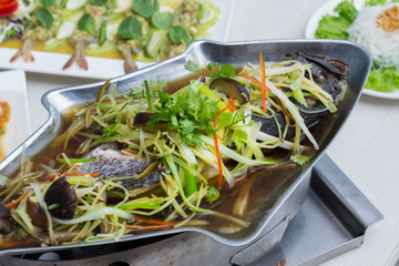 Steamed grouper with soy sauce in fish shape pot on the table with other food.
