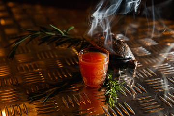 An underexposed horizontal image of an orange shot drink, decorated with fuming rosemary. Turtle...