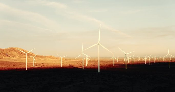 Aerial silhouette of wind turbines spinning at sunset in desert