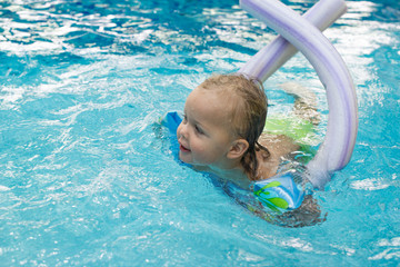 Happy little girl learning to swim with pool noodle