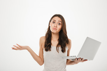 Photo of upset woman with long brown hair throwing up hands and expressing confusion while holding silver personal computer, isolated over white wall