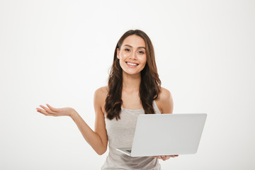 Naklejka premium Image of amazing businesswoman holding silver laptop and gesturing with smile, over white wall