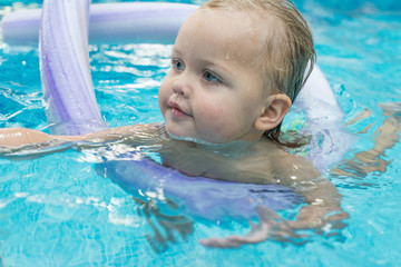 Happy little girl learning to swim with pool noodle
