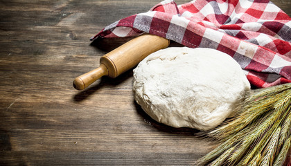 Dough with a rolling pin and spikelets of wheat.