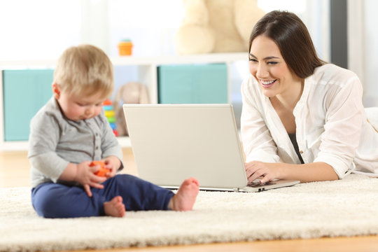 Mother working with a laptop and baby playing