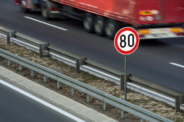 Traffic sign showing speed limit on a highway with truck driving in the background