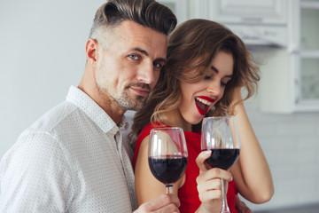 Photo of handsome man hug his woman and looking camera while drinking wine
