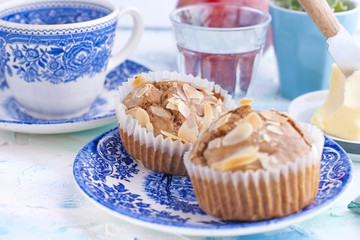 Homemade sweet muffins with almonds for breakfast. Tea and a glass of water in vintage blue dishes. Fruit and oil. Free space for text or a postcard.