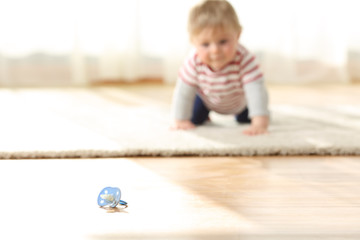 Naklejka premium Baby crawling towards a dirty pacifier on the floor