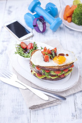 Toast from a grain bread with cheese and tomatoes and egg. Vegetarian food. on a white plate and blue dumbbells and a fitness bracelet for fitness. Phone. Useful breakfast. Free space for writing text