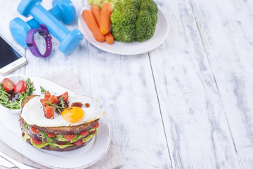 Toast from a grain bread with cheese and tomatoes and egg. Vegetarian food. on a white plate and blue dumbbells and a fitness bracelet for fitness. Phone. Useful breakfast. Free space for writing text