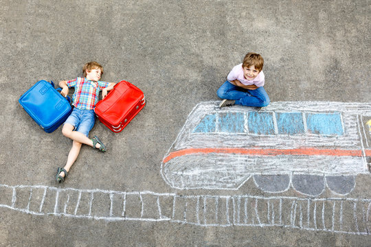 Two little kids boys having fun with train picture drawing with colorful chalks on ground