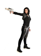 full length portrait of black haired girl wearing leather outfit. standing pose while holding a gun, isolated on a white studio background.