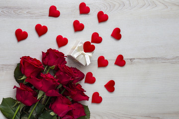 on a light wooden table, red roses, decor in the form of hearts and a gift box