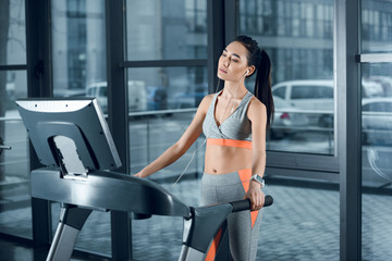 young athletic sportswoman jogging on treadmill and listening music with earphones at gym