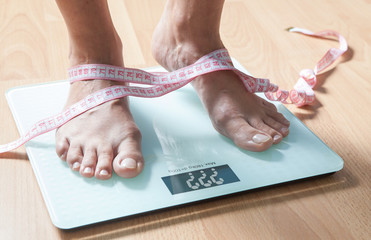 Healthy diet, fitness and weight loss concept. The legs of a young woman on the scales. Measuring tape. Checking the weight.