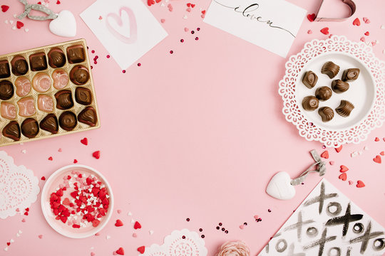 Valentine's Day, love concept. Mock up frame made of confetti, heart symbol accessories, sweets, postcards on pink background. Flat lay, top view.