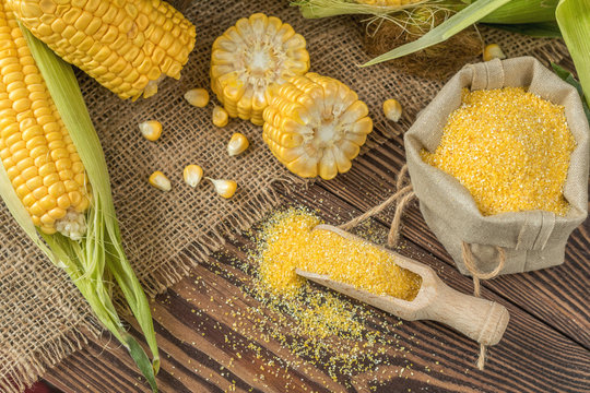 Fresh corn on cobs on rustic wooden table, top view. Dark wooden background freshly harvested organic corn. Corn grits in cloth sack.