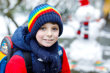 Happy kid boy with glasses having fun with snow on way to school, elementary class