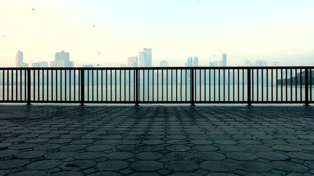 Background for opener. Landscape with the tile and fance at quay and the seaside skyscrapers in the summer. Misty day blue sky city skyline.