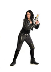 full length portrait of black haired girl wearing leather outfit. standing pose while holding a gun, isolated on a white studio background.