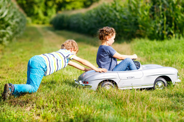 Fototapeta premium Two happy children playing with big old toy car in summer garden, outdoor