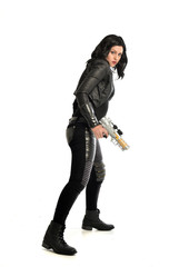 Naklejka premium full length portrait of black haired girl wearing leather outfit. standing pose while holding a gun, isolated on a white studio background.