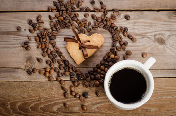 The cup of coffe and Frame- heart from coffee beans and two cookies-heart related together inside it on  wooden table
