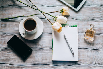 Woman's workplace top view. Notebook, pen, flowers, perfume, tablet and phone on a wooden table