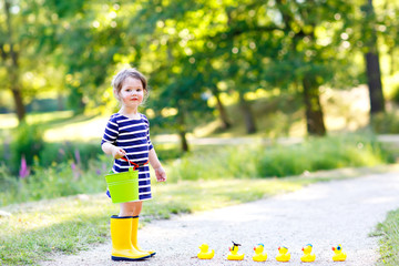 Beautiful little toddler girl playing in park. Adorable child wearing fashion casual clothes and yellow rubber boots.