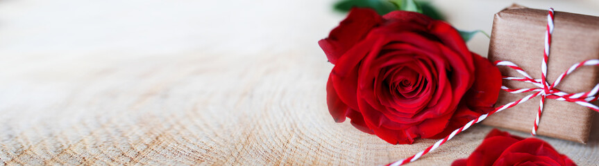Red roses with a gift on bright rustic wood