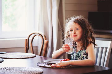 happy 8 years old child girl having breakfast in country kitchen, drinking milk and eating toast with strawberry