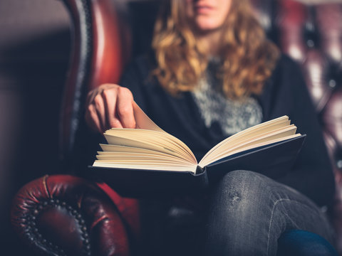 Young woman on leather sofa reading a book