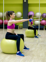 Young model girl makes exercises at the gym in front of mirror