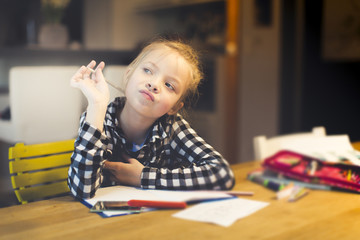 beautiful, blond girl is sitting at the table and is doing schoolwork at home