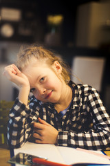 beautiful, blond girl is sitting at the table and is doing schoolwork at home