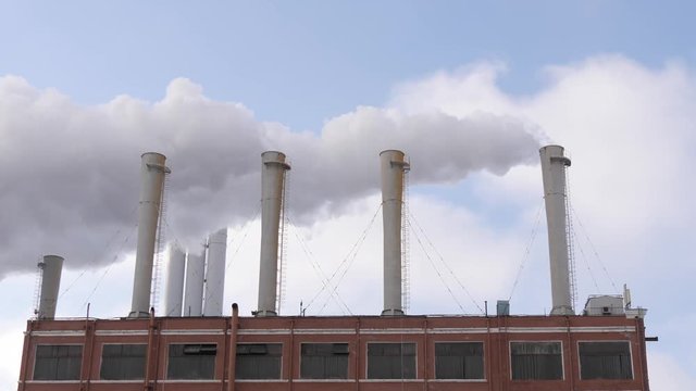 Industrial site with smoking pipes with blue sky on background. Global warming concept, ecology problem. 4k slow motion.
