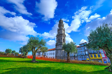 Fototapeta na wymiar Bell tower of the Clerigos Church (Church of the Clergymen), a baroque church in backlit winter sunbeam. Old olive trees and green grass lawn on foreground. City of Porto, in Portugal.