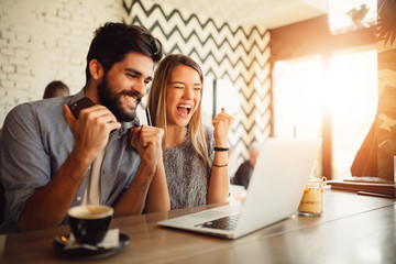 Surprised young couple doing online shopping through laptop and credit card at cafe.