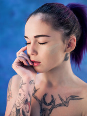 Obraz premium Beautiful girl with dyed hair and tattooes posing in studio on blue background