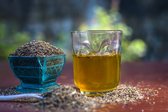 Black cumin seeds,shah jerra,Nigella sativa  and its extracted water in a transparent glass on brown wooden surface.;