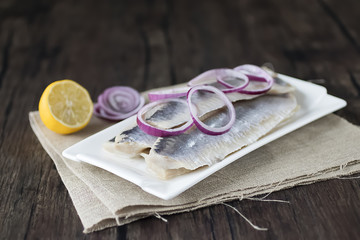Herring fillets in a white plate on a dark wooden table.