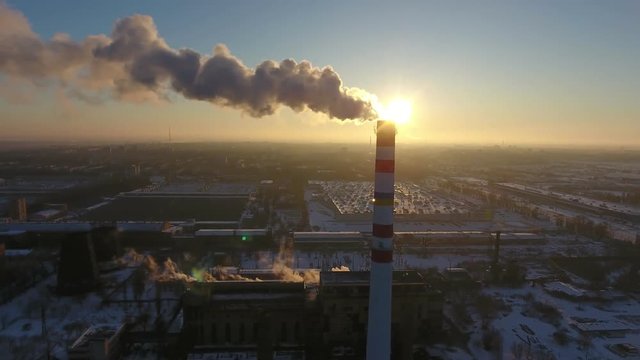 A bird`s eye view of a sky- high chimney with a slow stream of smoke at a wonderful sunset in winter. The cityscape is picturesque