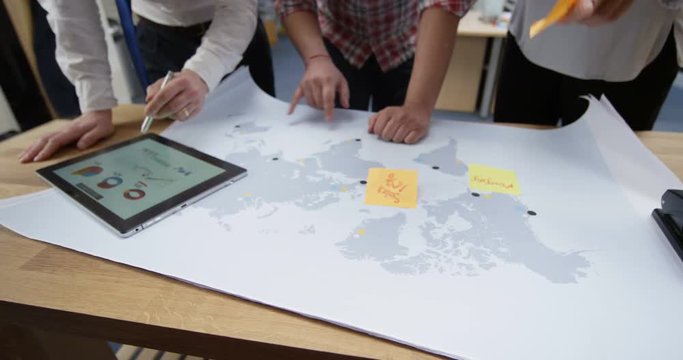 4K Business partners with startup company looking at world map & tablet, strategizing their business development. Slow motion.